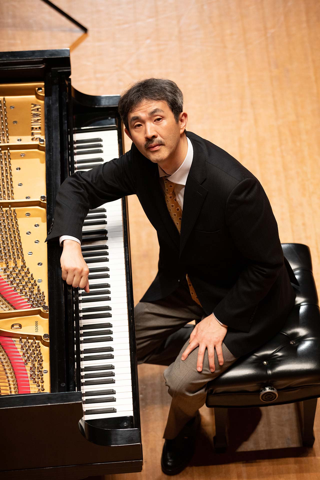 戸口 純がピアノの前に座るフォーマルな公演ポートレート